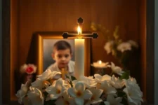 Cómo Integrar esta Oración Milagrosa para la Salud de un Hijo en Tu Vida Diaria, muestra una vela encendida frente a una cruz y un retrato de un niño, rodeada de flores blancas en un altar íntimo y cálido.