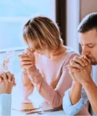 Cómo Integrar esta Oración del Padre Pío por la Familia en Tu Vida Diaria Familia reunida en oración alrededor de una mesa, fondo con cruz y muebles rústicos.