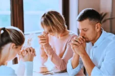 Cómo Integrar esta Oración del Padre Pío por la Familia en Tu Vida Diaria Familia reunida en oración alrededor de una mesa, fondo con cruz y muebles rústicos.