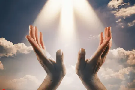La Oración de Fe Sanará al Enfermo 5 Interpretación de La Oración de Fe Sanará al Enfermo, muestra manos levantadas hacia un rayo de luz brillante en un cielo azul con nubes.
