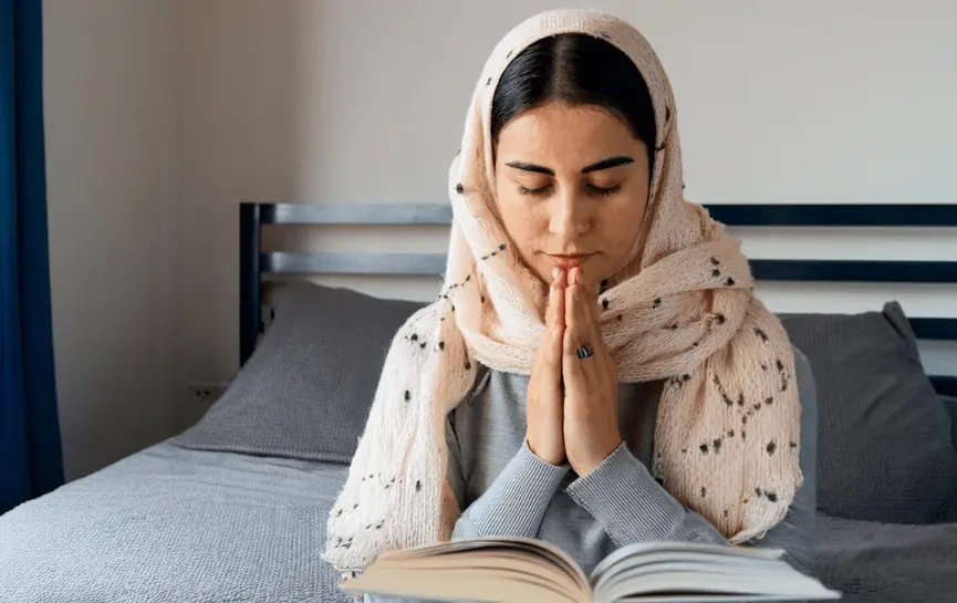 Oraciones para Pedir la Salud de un Enfermo, muestra a una mujer con un pañuelo estampado en la cabeza, con las manos juntas en actitud de oración sobre un libro, sentada en una cama.