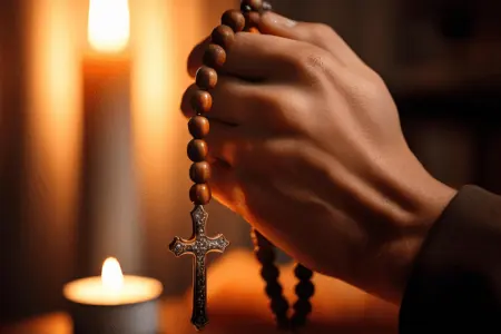 Novena a San Gregorio para la Salud 1 Oración a San Gregorio para la Salud, muestra manos sosteniendo un rosario con una cruz metálica, iluminadas por la luz cálida de velas en un ambiente oscuro y sereno.